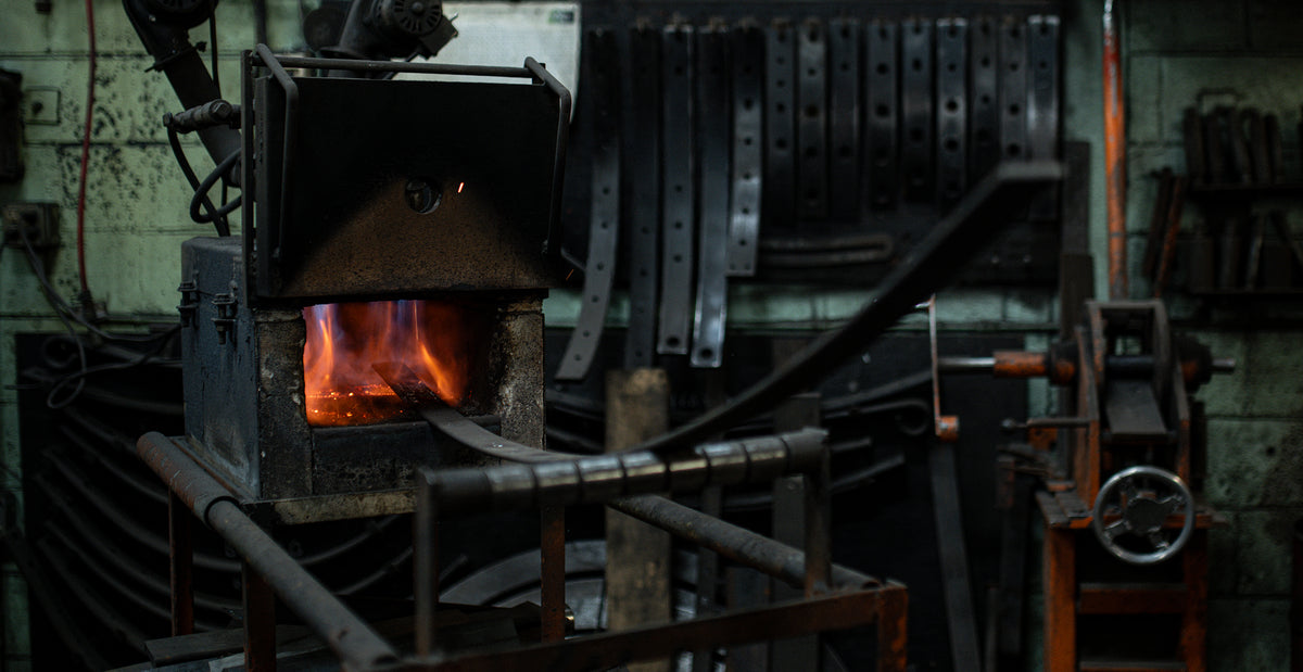 Forge industrielle chauffant une lame de ressort en acier chez Edgar Blondeau, illustrant la maîtrise technique de la fabrication sur mesure pour suspensions lourdes à Québec.
