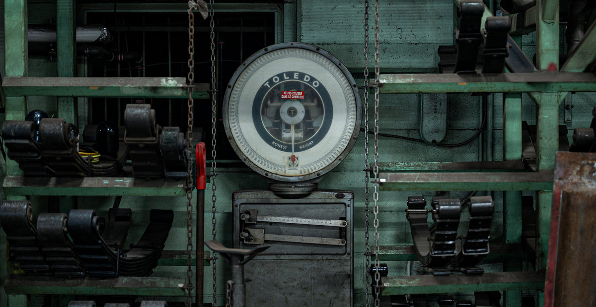 Balance industrielle vintage Toledo entourée de lames de ressort numérotées dans l'atelier historique d'Edgar Blondeau, spécialiste en suspension de camions à Québec.