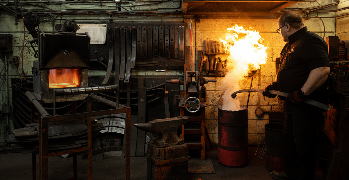 Fabrication sur mesure : Expert d'Edgar Blondeau procédant à la trempe d'un ressort à lames sur mesure, illustrant la maîtrise de notre forge exclusive pour véhicules lourds à Québec.